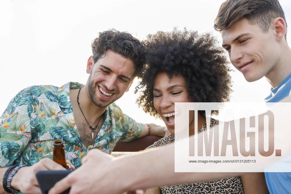 IMAGO Creative: Landleben - Alfresco, Draußen Cheerful male and female friends sharing smart phone during weekend party model released Symbolfoto property released IFRF00998