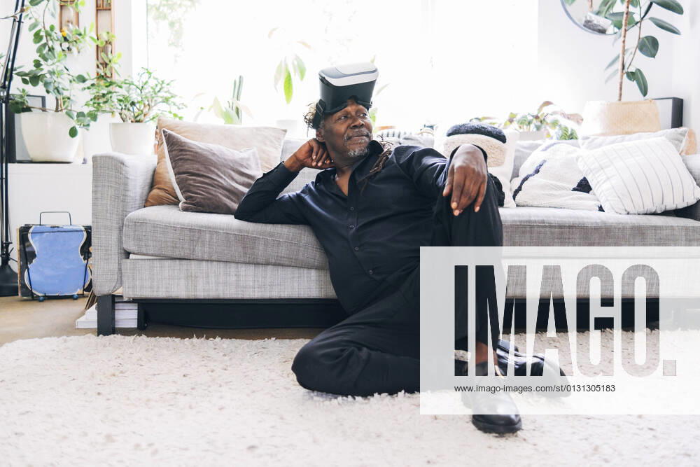 Relaxed man with virtual reality headset looking away while leaning on sofa at home model released Symbolfoto property released ASGF01083
