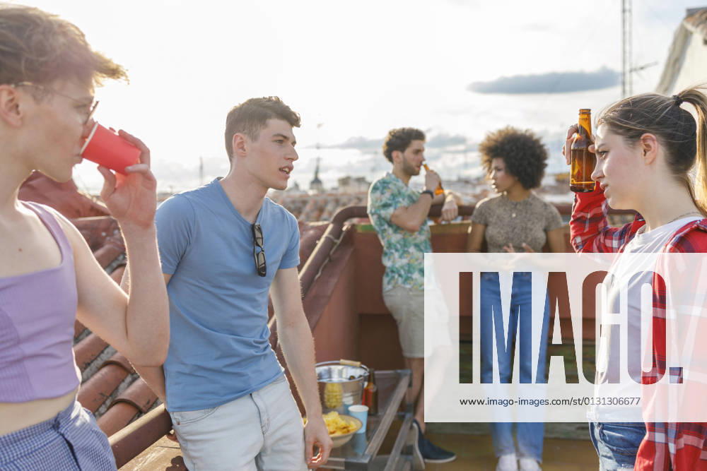 IMAGO Creative, Urban Lifestyle Multi-ethnic friends talking while having drinks on terrace during party model released Symbolfoto property released IFRF00994