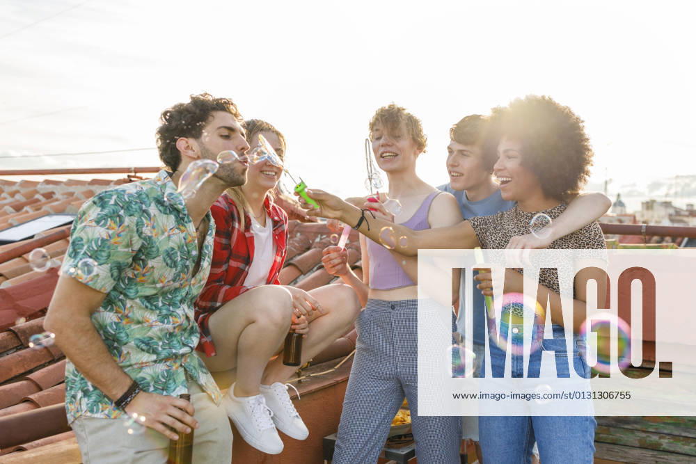 Cheerful young male and female friends blowing bubbles together on rooftop model released Symbolfoto property released IFRF01022
