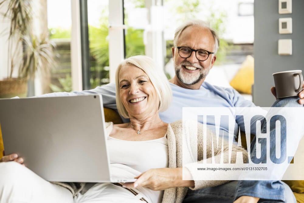 IMAGO Creative: Jahreszeit Winter, Couching Woman smiling at video call through laptop while sitting with man on sofa model released Symbolfoto property released UUF24074