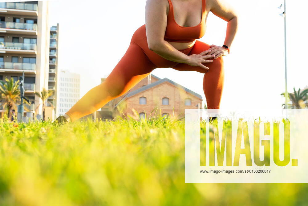 IMAGO Creative, Jahreszeit Sommer, Sommer in der Stadt Ground level of crop anonymous plump female athlete working out on lawn against urban buildings in sunlight DavidMunoz_MontseSport_43.jpg