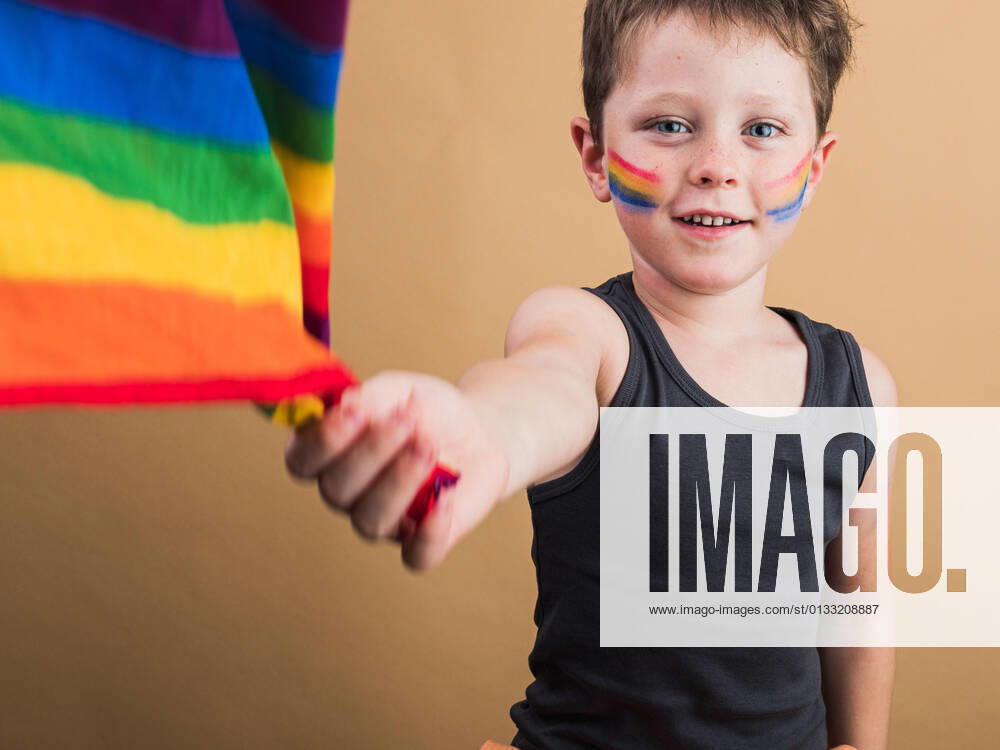 IMAGO Creative: Pride Month 2022, Engagement der Jugendlichen Cheerful kid with makeup on cheeks with LGBTQ flag while looking at camera on beige background HodeiUnzueta_EtxahumStudioConcepts_59.jpg