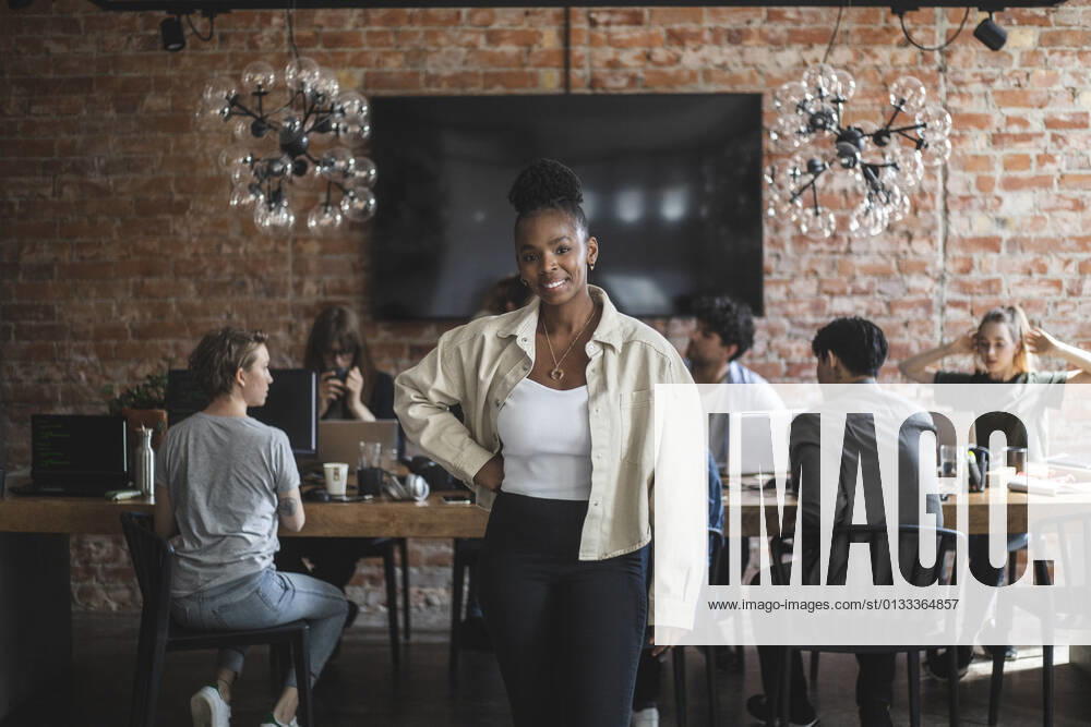 Female entrepreneur standing with arms crossed while colleagues working in creative office Sweden, Stockholm, model released, property released