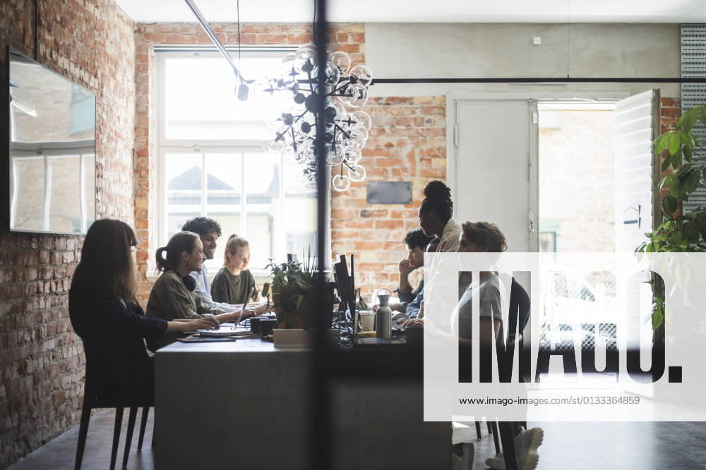 Female entrepreneur standing with arms crossed while colleagues working in creative office Sweden, Stockholm, model released, property released