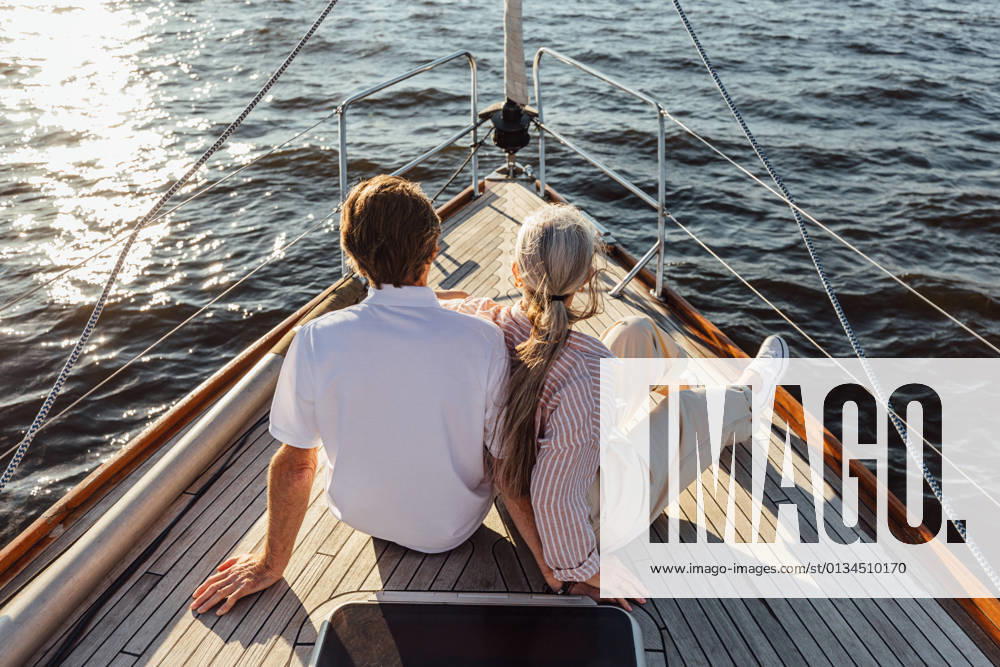 Rearview of two mature people sitting on a yacht bow. Loving senior couple enjoying a boat trip. Rearview of two mature people sitting on a yacht bow. Loving senior couple enjoying a boat trip.