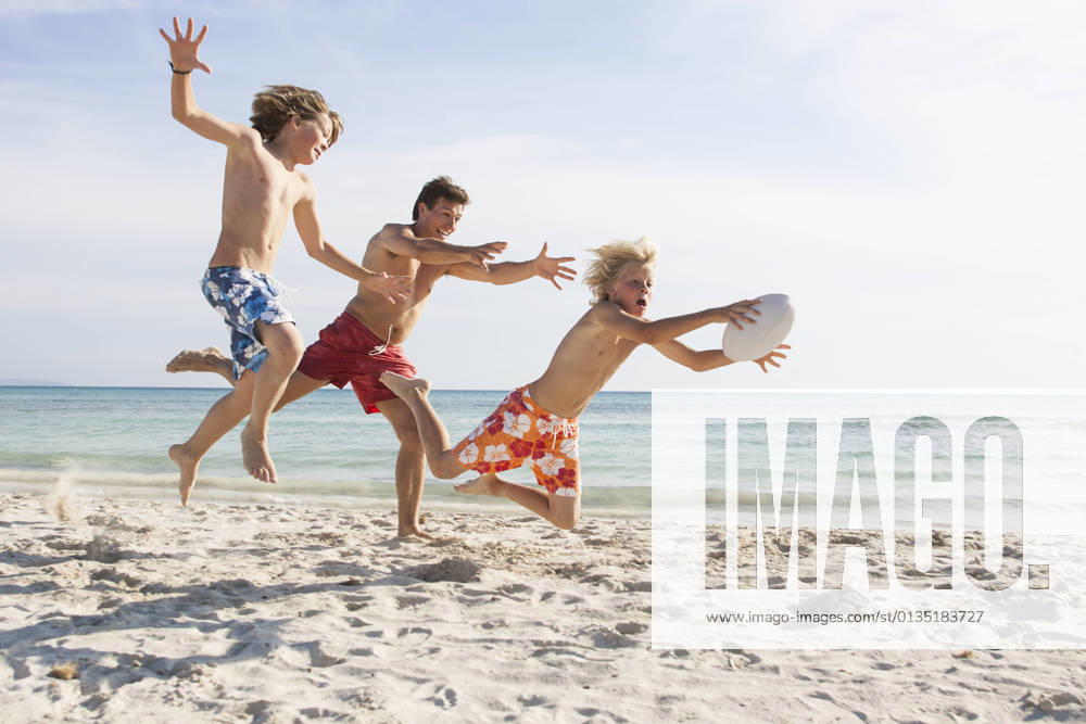Boy and father chasing brother with rugby ball on beach, Majorca, Spain, 13.04.2016,