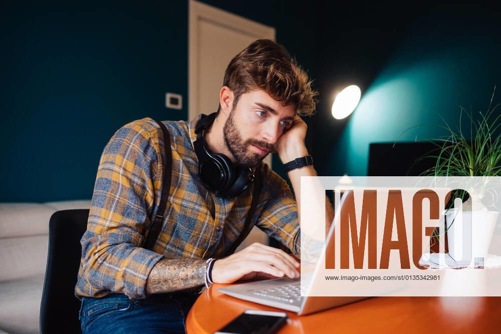 Mid adult man sitting at living room table looking at laptop, 25.04.2019,