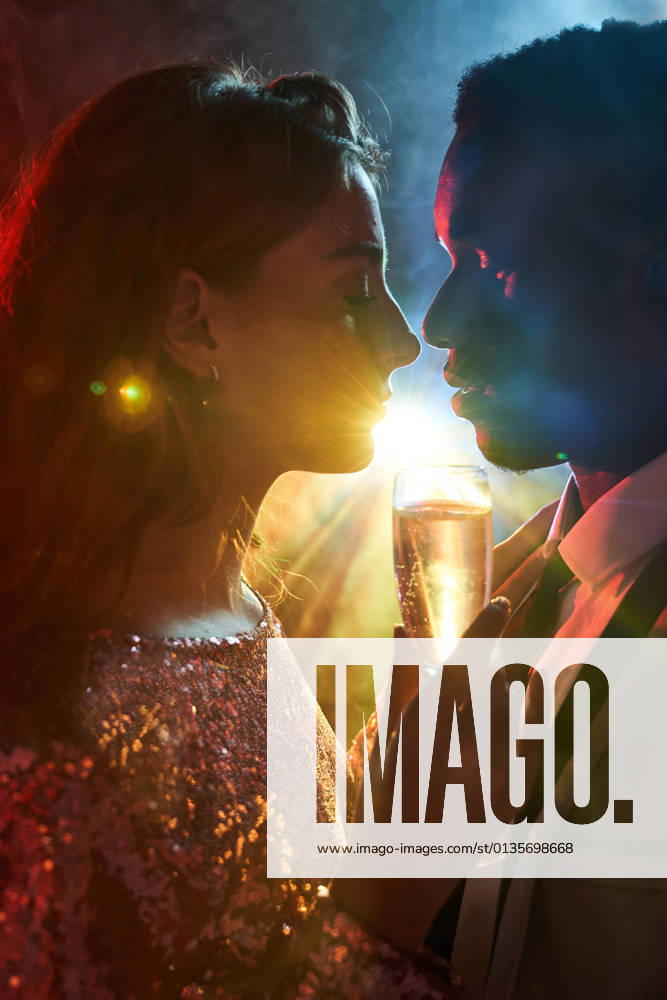 Side view of crop couple with glass on champagne in moment of kiss against shiny light ray looking at each other during party ManuelRuiz_NewYearsEvePartyCouple_31.jpg