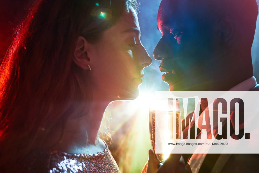Side view of crop couple with glass on champagne in moment of kiss against shiny light ray looking at each other during party ManuelRuiz_NewYearsEvePartyCouple_32.jpg