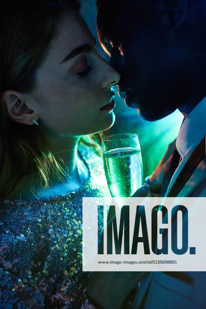 Side view of crop couple with glass on champagne in moment of kiss against shiny light ray looking at each other during party ManuelRuiz_NewYearsEvePartyCouple_34.jpg
