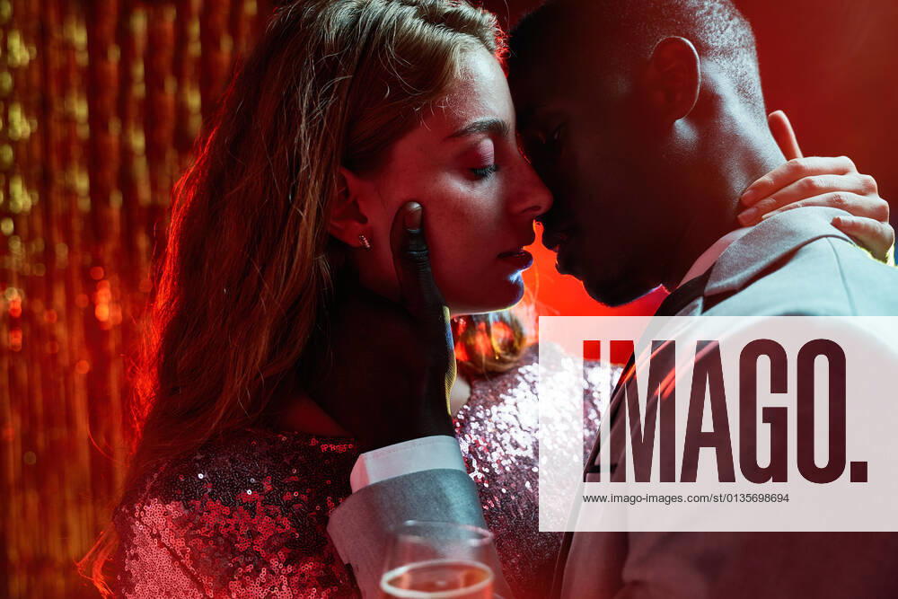 Side view of crop couple with glass on champagne in moment of kiss against shiny light ray looking at each other during party ManuelRuiz_NewYearsEvePartyCouple_35.jpg