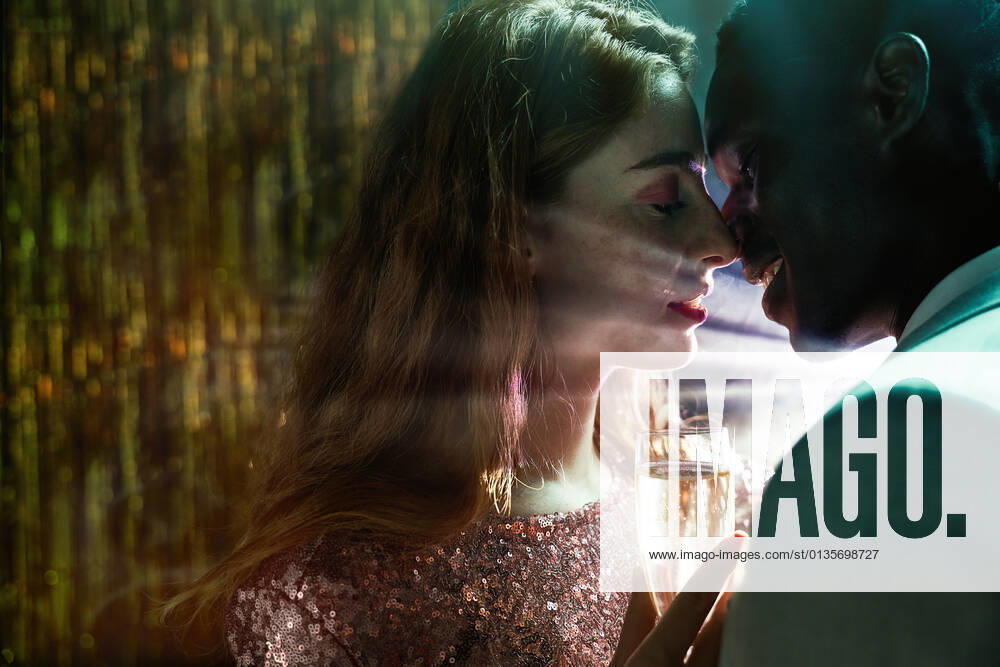Side view of crop couple with glass on champagne in moment of kiss against shiny light ray looking at each other during party ManuelRuiz_NewYearsEvePartyCouple_37.jpg