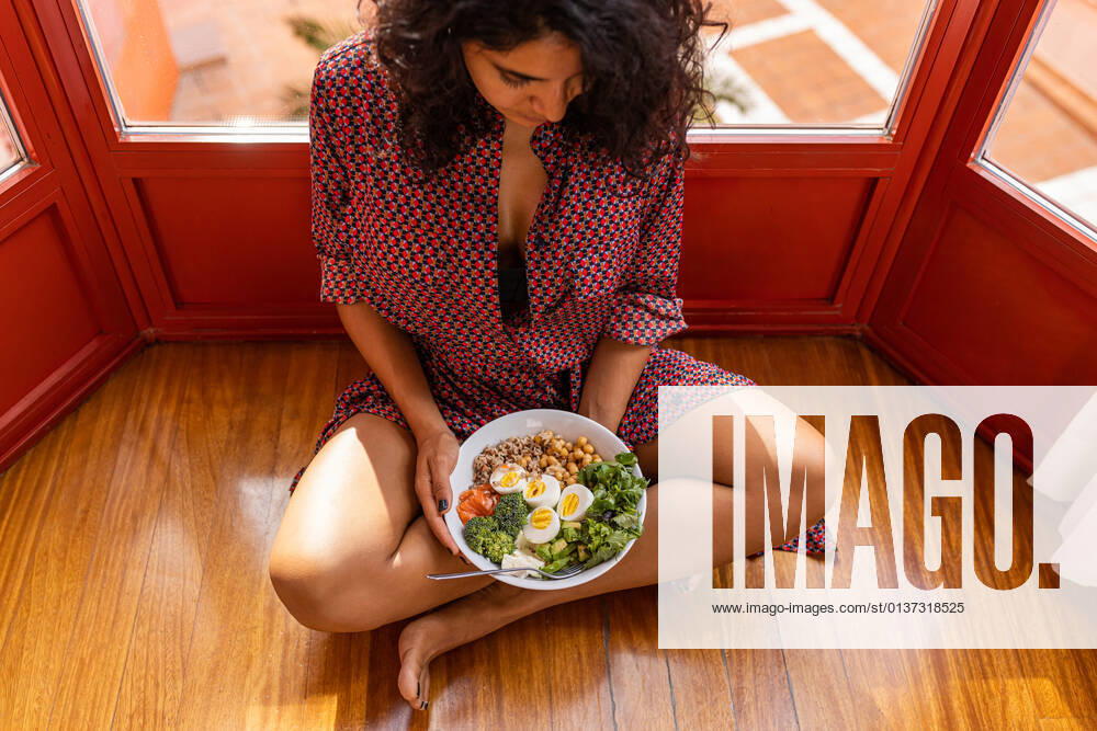 High angle of young female with curly hair sitting with crossed legs and eating super food bowl with chickpea chopped eggs broccoli DavidFuentes_HealthyFood_22.jpg