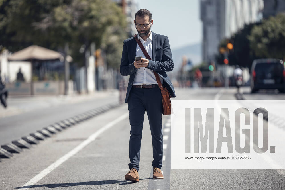 Male business professional using mobile phone while walking in city model released Symbolfoto JSRF01648