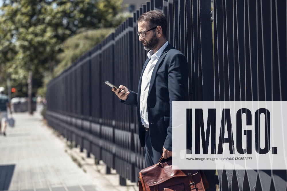 Male business professional using mobile phone on footpath model released Symbolfoto JSRF01657