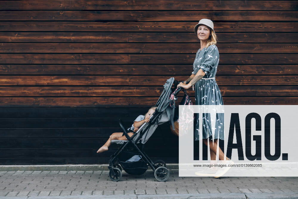 Mid adult woman pushing baby stroller on footpath model released Symbolfoto OMIF00073
