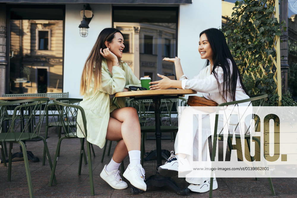 Smiling female friends talking at sidewalk cafe model released Symbolfoto OYF00539