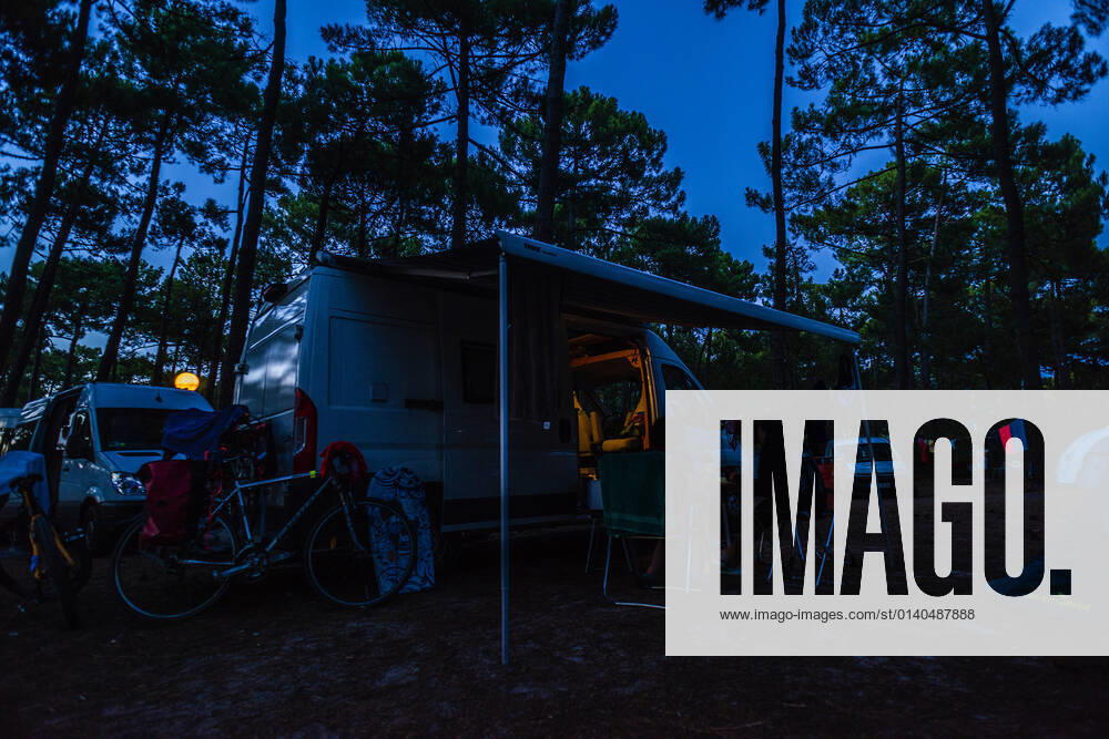 Camper sitzen zur blauen Stunde an einem lauen Sommerabend vor ihrem Camper auf Campingstühlen auf einem Campingplatz. Bordeaux (Gironde), Nouvelle Aquitaine, Frankreich. Mit einem Campervan unterwegs