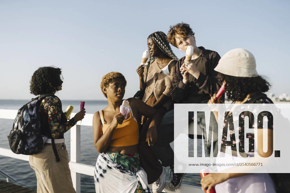 IMAGO Creative: Frauenmonat im März IMAGO Creative: Digitale Welt, Verzicht auf Technologie LGBTQIA multiracial friends eating ice creams on railing during sunny day Sweden, Malmo, model released