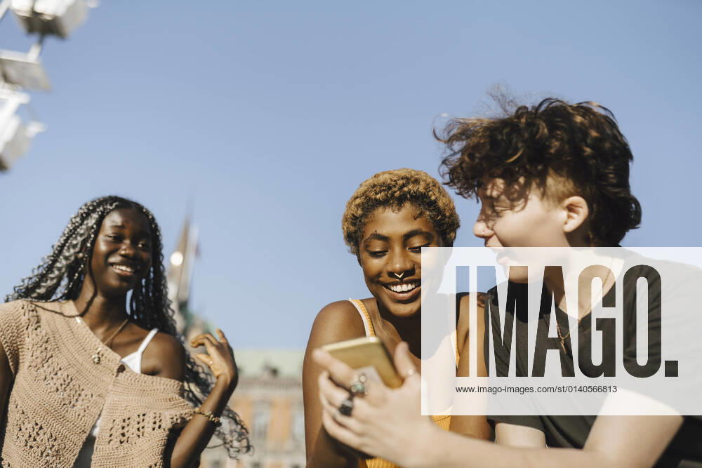 IMAGO Creative: Pride Month 2022, Engagement der Jugendlichen Teenage boy sharing smart phone to young friends on sunny day Sweden, Malmo, model released