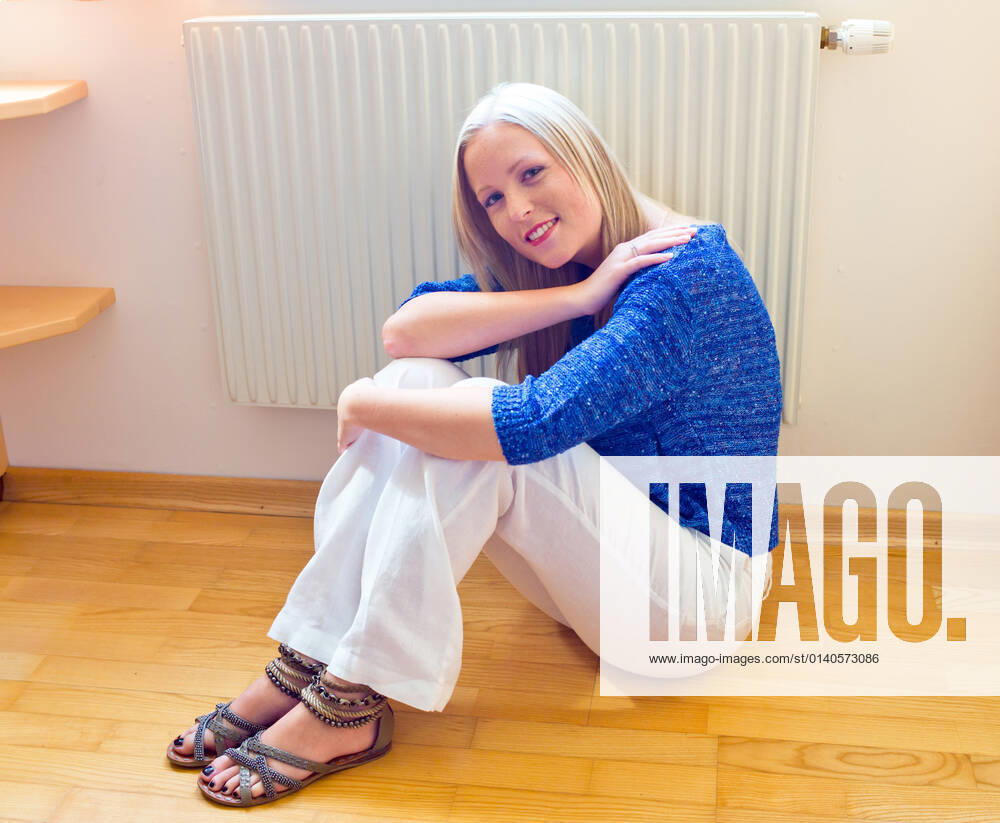 Eine junge Frau sitzt im Winter vor einem Heizkörper. Raumtemperatur ist zu niedrig. McPBBO