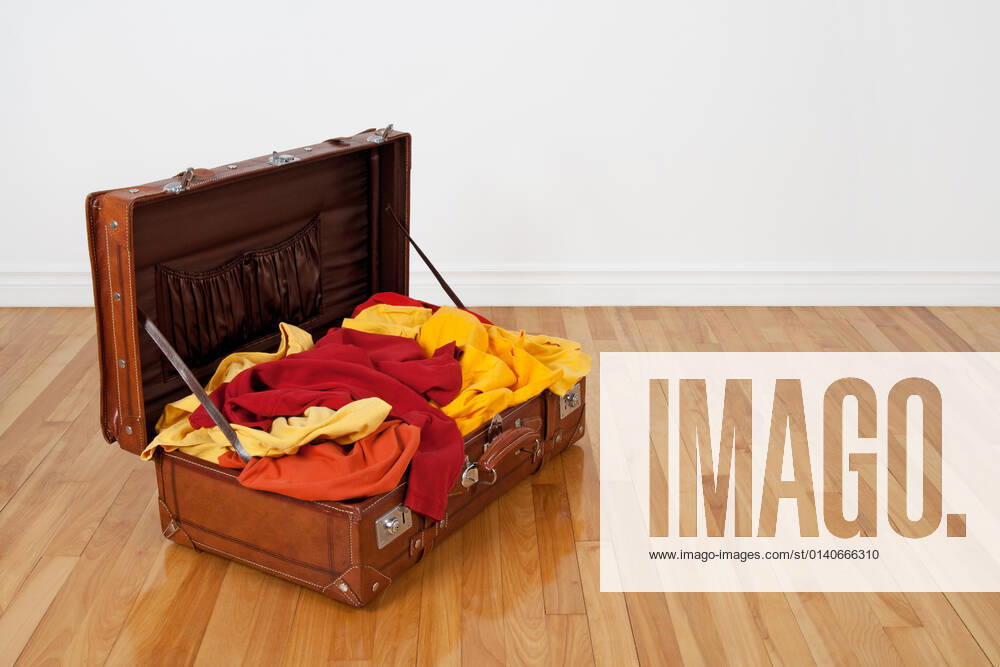 Leather suitcase on the wooden floor, full of orange, red and yellow clothing.