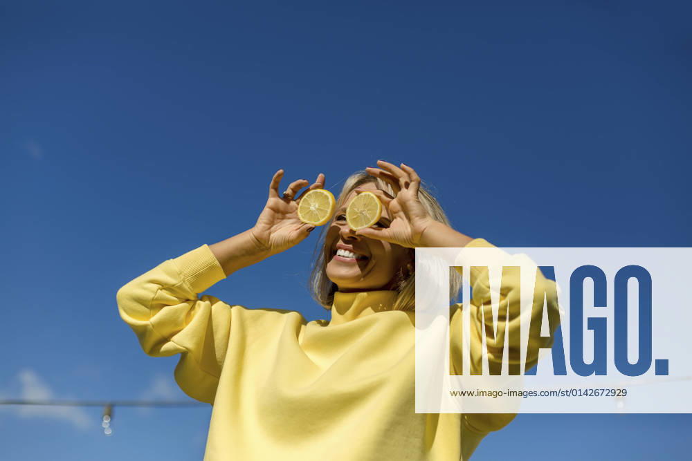 Cheerful woman holding slice of lemon in front of eyes during sunny day model released, LLUF00168