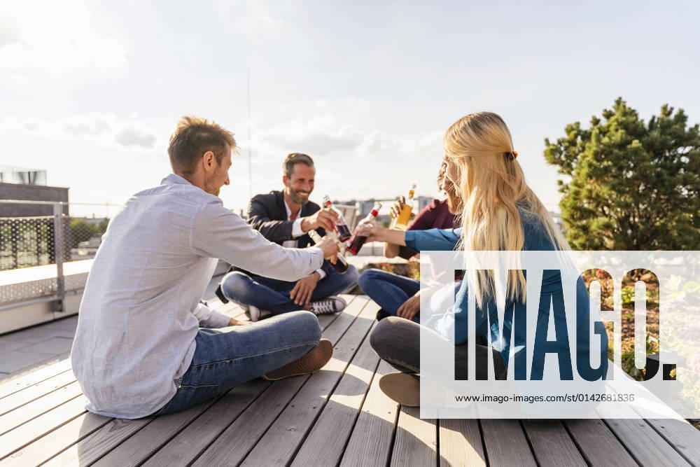 IMAGO Kreativ: Urbane Kultur - Sommer auf den Dächern Coworkers toasting drinks while sitting on rooftop model released property released, DIGF16937