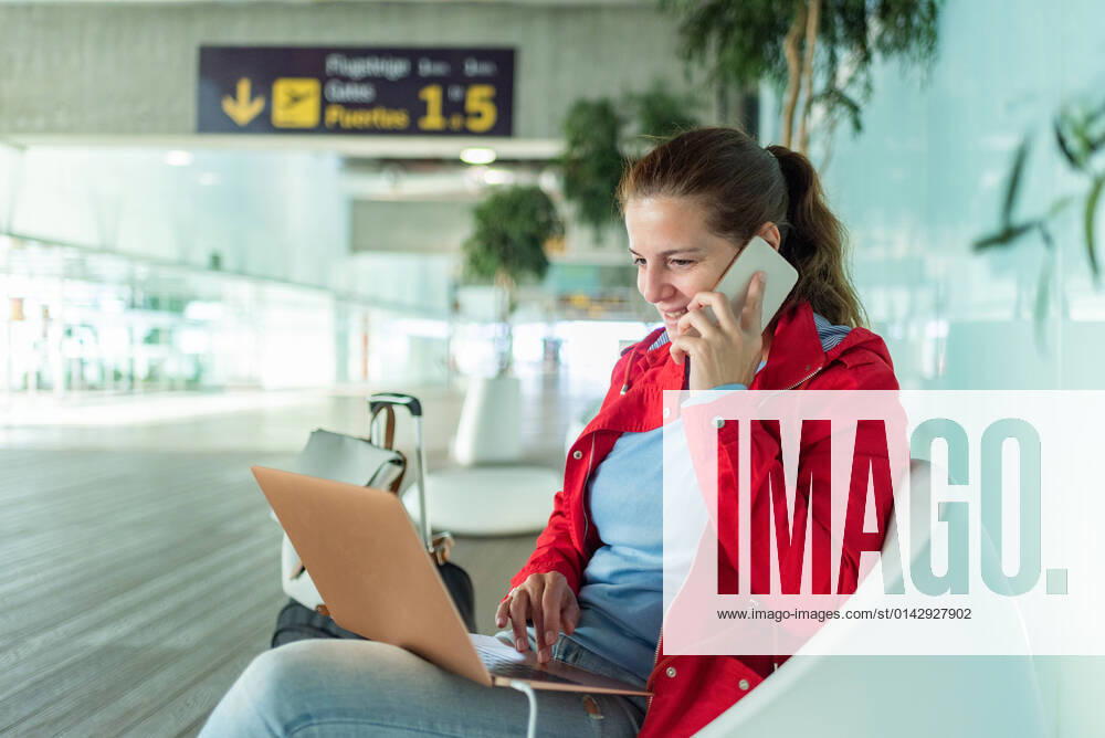 IMAGO Creative: Fr?hlingsferien und reisen Positive female traveler with cellphone on a phone call while on internet on netbook sitting in armchair near suitcase in light modern airport terminal GabrielTrujillo_La PalmaAirport_28.jpg