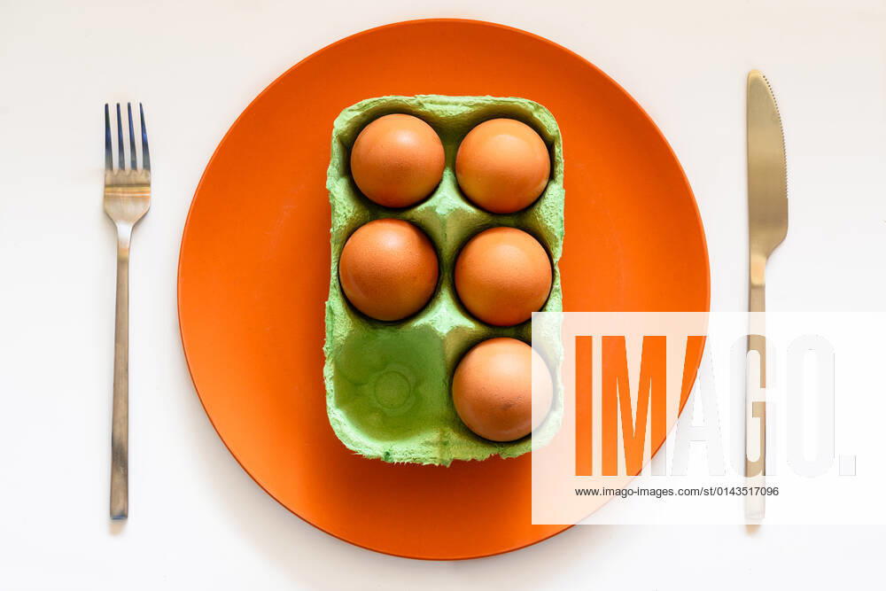 Top view of carton box of eggs placed on orange ceramic plate on white table with knife and fork JavierDeLaTorre_MinimalistFood_10.jpg