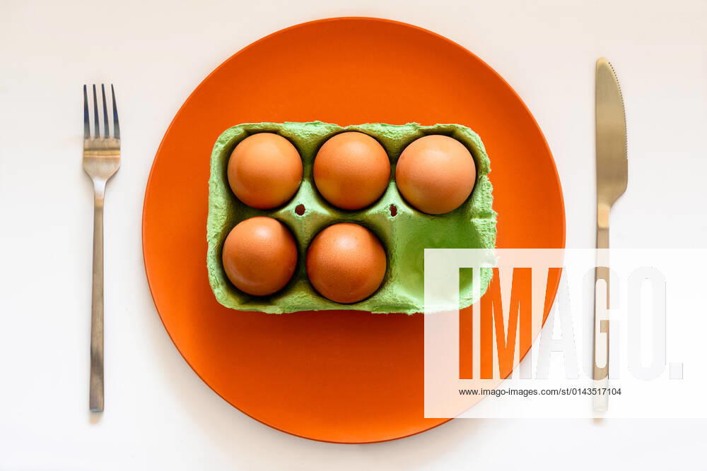 Top view of carton box of eggs placed on orange ceramic plate on white table with knife and fork JavierDeLaTorre_MinimalistFood_17.jpg