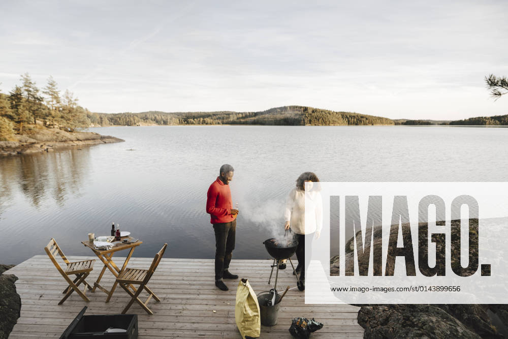 Full length of couple preparing food on barbecue grill against lake Sweden, Dalsland, model released