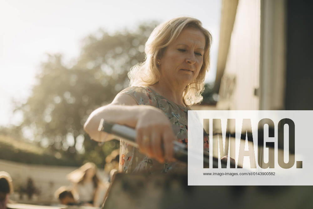 IMAGO Creative: Landleben - Essen IMAGO Creative: Landleben - Alfresco, Draußen Mature woman preparing food on barbecue grill during dinner party Sweden, Stockholm, model released, property released