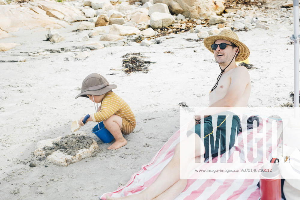Smiling man by son playing on sand at beach model released, Gloucester Massachusetts USA ACTF00163