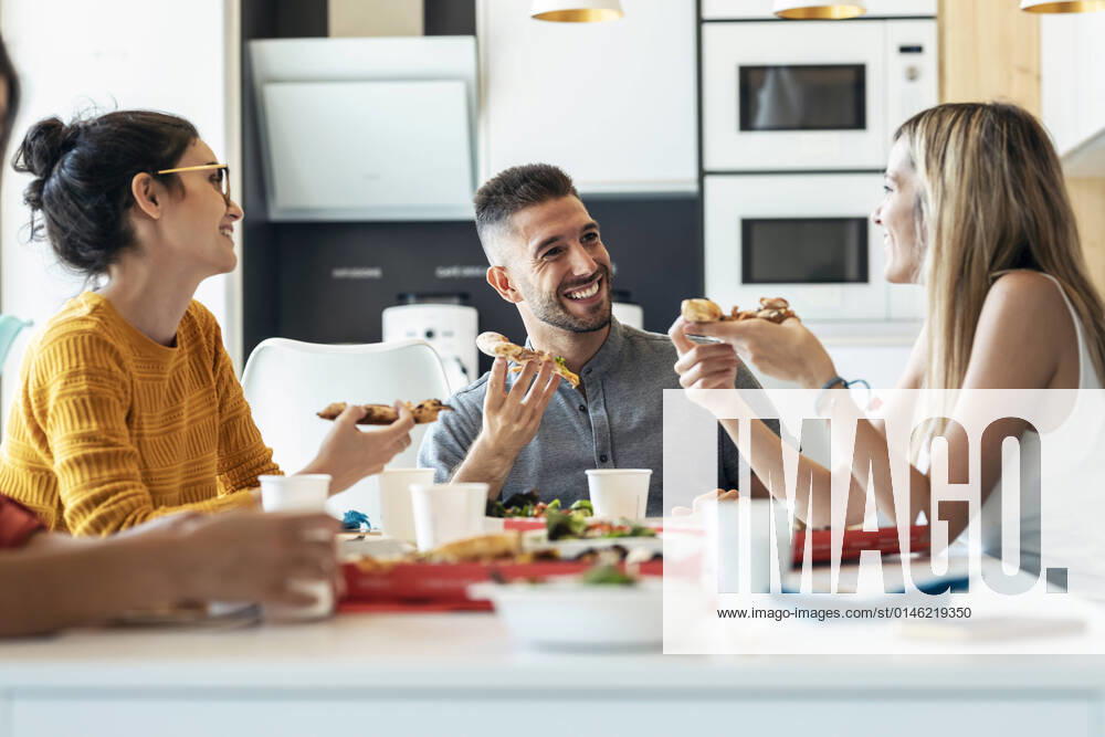 IMAGO Creative: Gesellschaft, Integration Smiling businessman with pizza talking to businesswoman at office cafeteria model released property released, JSRF01725
