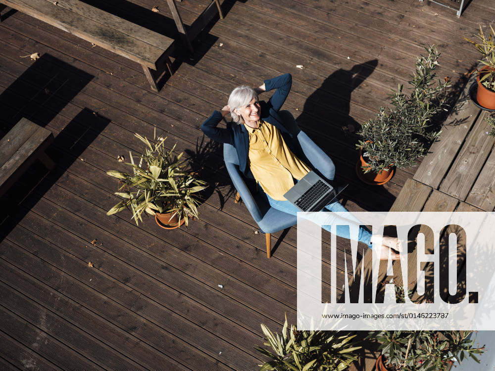 IMAGO Kreativ: Urbane Kultur - Sommer auf den Dächern Businesswoman with hands behind head resting on armchair at rooftop model released property released, JOSEF06043