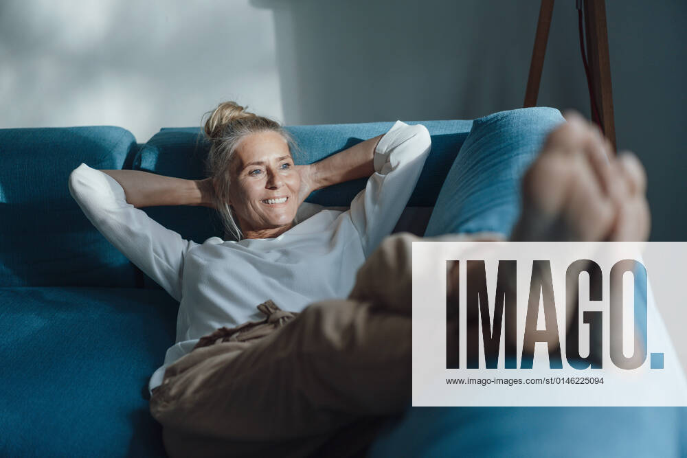 Smiling woman with hands behind head relaxing on sofa model released property released, JOSEF06163