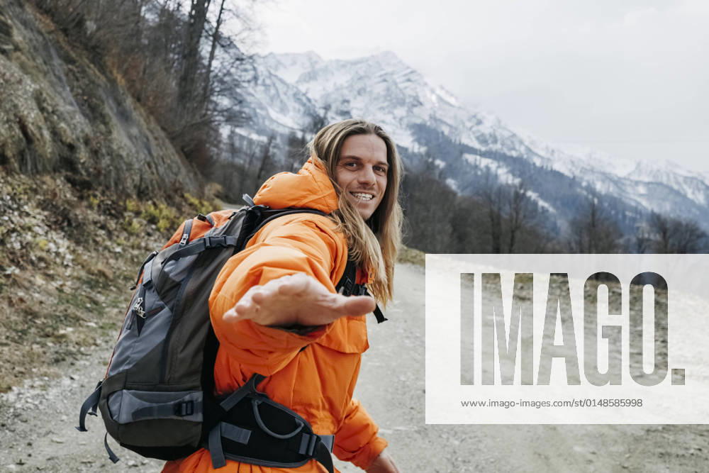 IMAGO Creative: 2022 Sport Favoriten IMAGO Creative: Wintersport, Urlaub Cheerful man in orange jacket walking on mountain road model released, OMIF00399