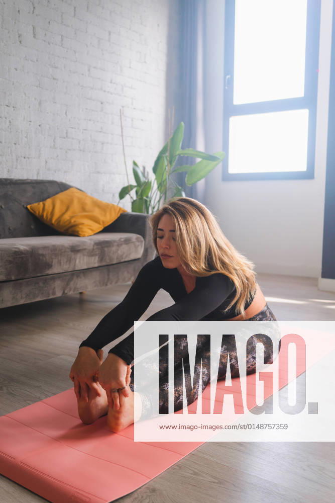 Full body of serene female stretching legs in Paschimottanasana pose while sitting on exercise mat in stylish room in morning, Model released MiguelPalomo_YogaAtMorning_6.jpg