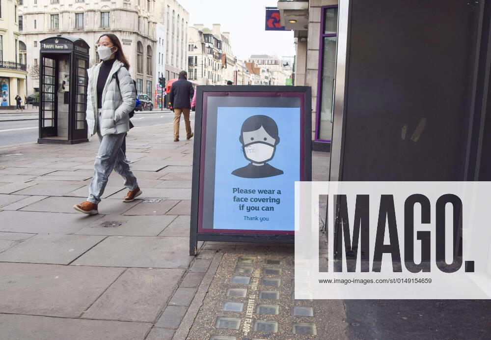 A woman wearing a face mask as a precaution against the spread of coronavirus walks past a sign outside a store in Central London encouraging people to continue to wear face masks if they can, as England ends mandatory face coverings in indoor public spaces. London United Kingdom - ZUMAs197 20220128_zaa_s197_114
