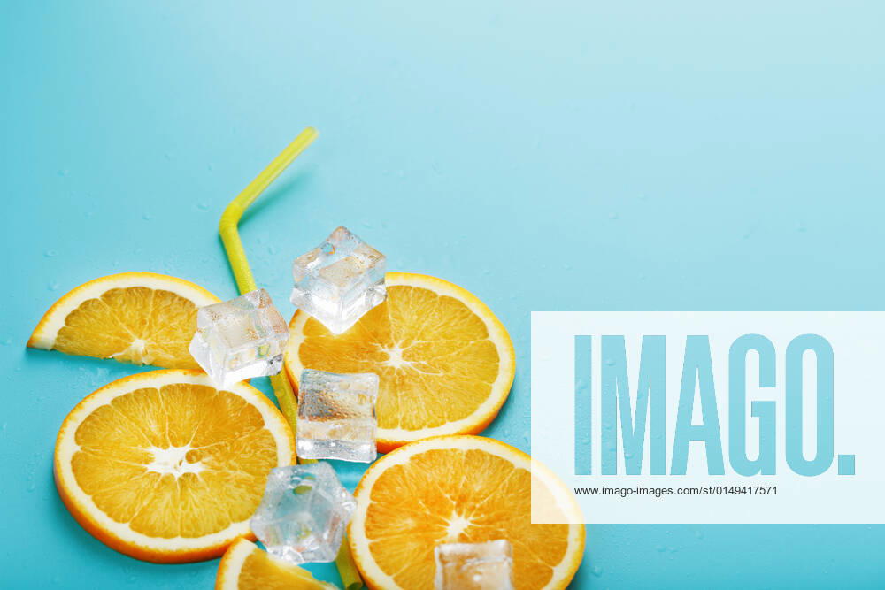 Orange slices and ice cubes with a straw on a blue background in the shape of a cocktail. Orange slices and ice cubes with a straw on a blue background in the shape of a cocktail. The concept of the drink lemonade is a summer refreshing composition. Top view