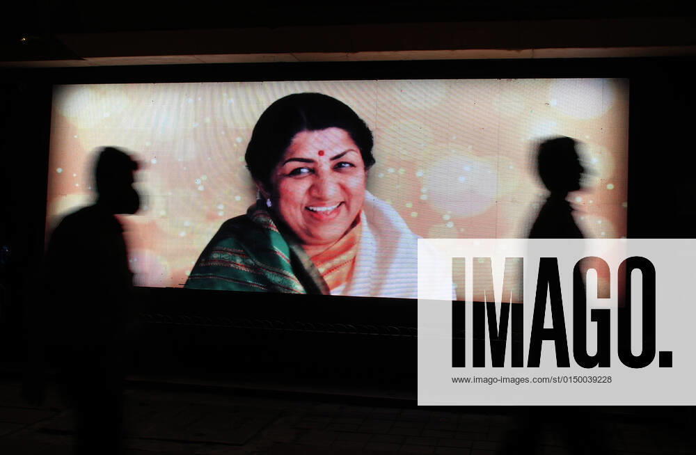 People walk past a LED display of legendary singer Lata Mangeshkar who passed away in Mumbai..The legendary singer was hospitalised and taken to an Intensive Care Unit (ICU) as her health deteriorated. she passed away on 6th February 2022 at the age of 92. Mumbai India - ZUMAs197 20220206_zaa_s197_287