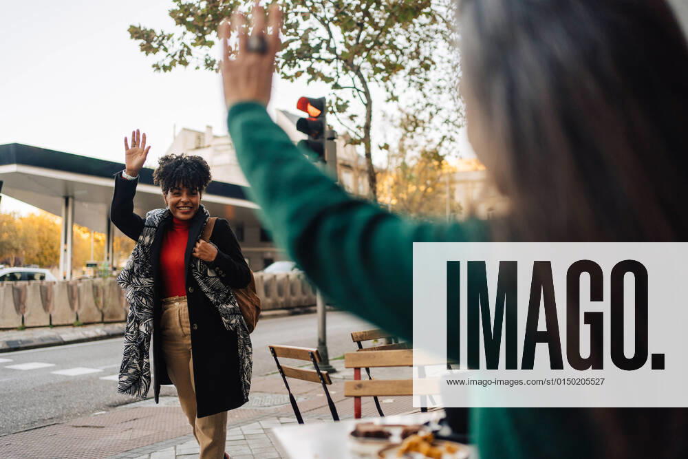 IMAGO Creative, Urban Lifestyle IMAGO Creative: Urban Diversity Hispanic female waving hand to excited African American friend while sitting at table with desserts in street cafe JakeJakab_EliAlicia_25.jpg