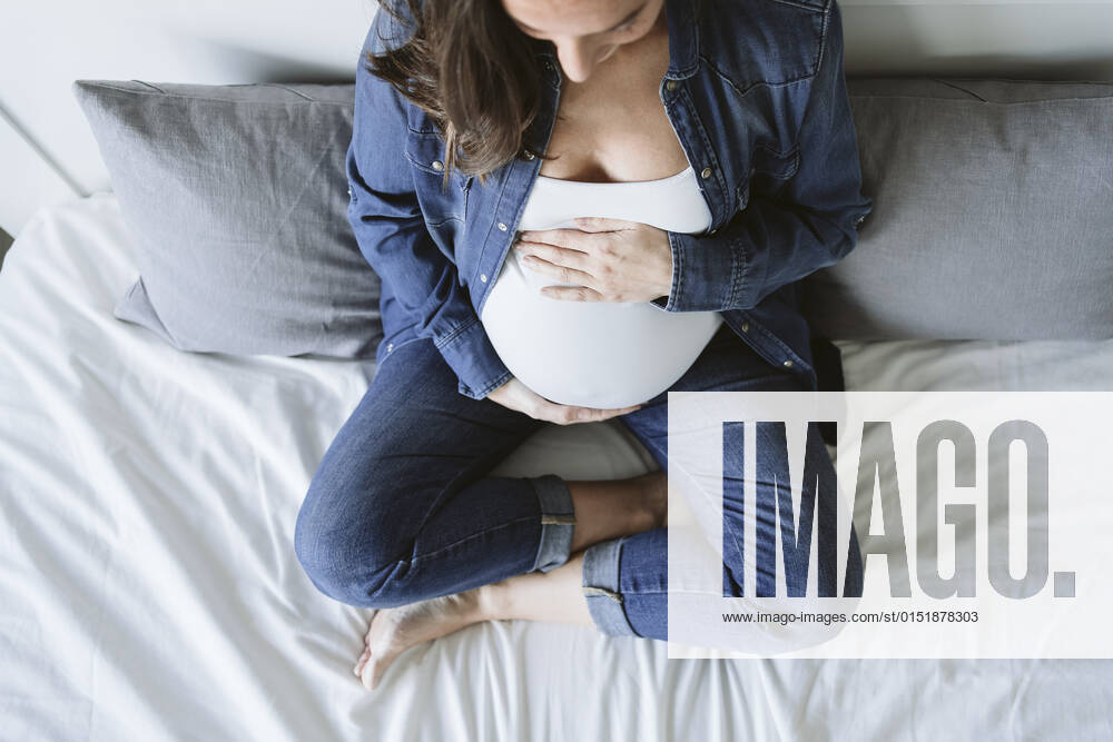Pregnant woman sitting on bed touching belly model released property released, EBBF05254