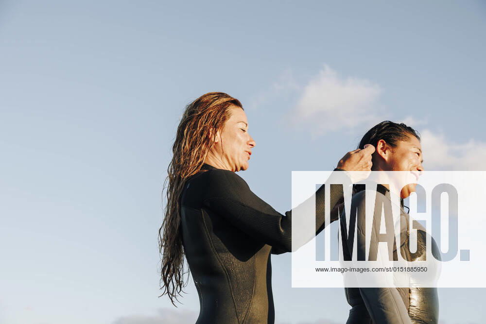 IMAGO Creative: 2022 Sport Favoriten IMAGO Creative: Frühlingsferien und reisen Smiling woman assisting surfer putting on wetsuit at beach model released, MRRF01901