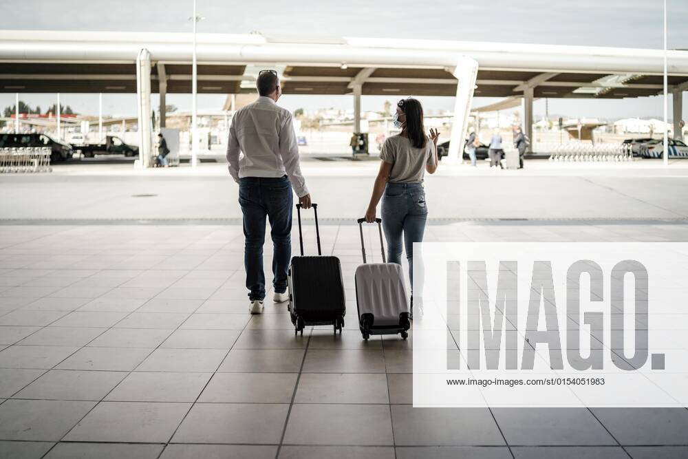 Ein paar Freunde mit Gepäck und Schutzmasken verlassen den Flughafen
