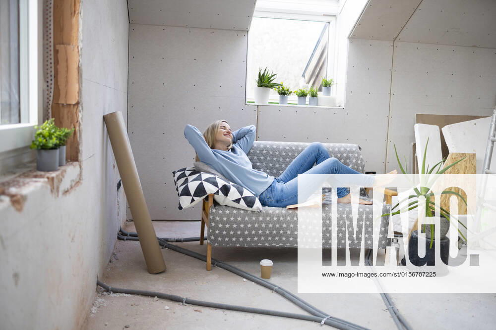 Smiling woman with hands behind head relaxing on sofa in attic model released, Symbolfoto property released, HMEF01347