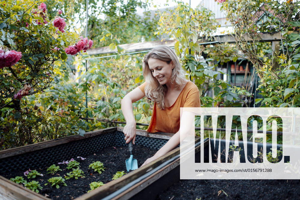 IMAGO Creative, Frühling, Start der Garten-Saison Smiling blond woman with shovel gardening in backyard model released, Symbolfoto property released, JOSEF08213