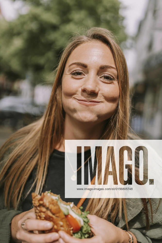 Smiling young woman with puffed cheeks eating sandwich model released, Symbolfoto, MFF09030